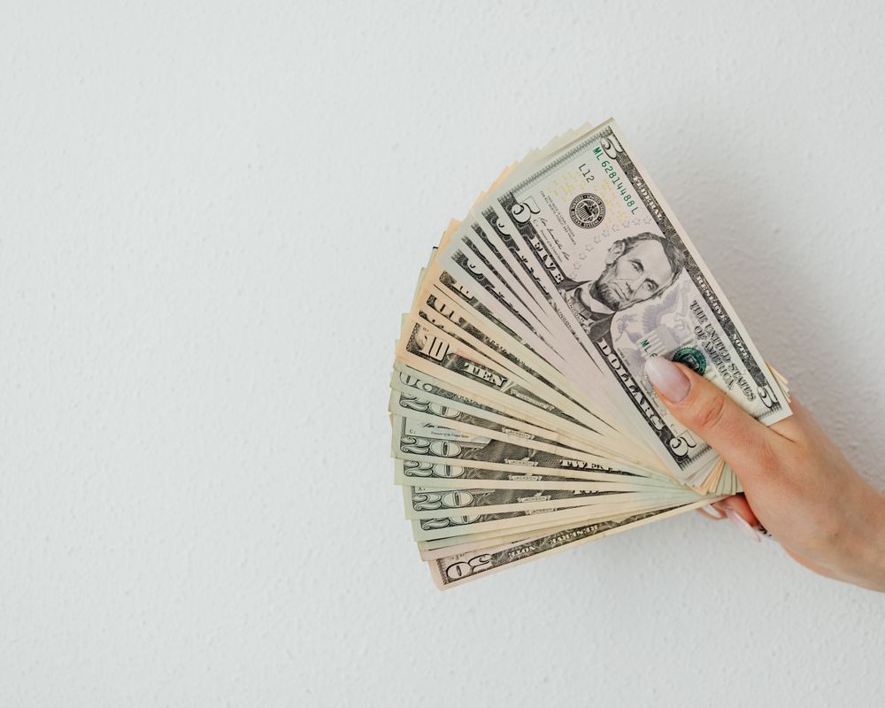 A hand holding a fan of US dollar bills against a clean white background